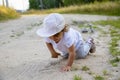 Cute happy toddler in a cap crawls on all fours along a country road in the sand on a sunny summer day Royalty Free Stock Photo