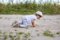 Cute happy toddler in a cap crawls on all fours along a country road in the sand on a sunny summer day Royalty Free Stock Photo