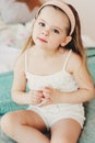 Cute happy toddler girl sitting on bed in pajama. Child playing at home