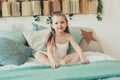 Cute happy toddler girl sitting on bed in pajama. Child playing at home