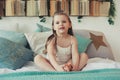 Cute happy toddler girl sitting on bed in pajama. Child playing at home