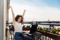 Cute happy young girl working on computer and smiling. Beautiful woman with laptop on a balcony with a landscape on the river Neva Royalty Free Stock Photo