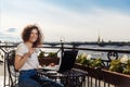 Cute happy young girl working on computer and smiling. Beautiful woman with laptop on a balcony with a landscape on the river Neva Royalty Free Stock Photo