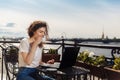 Cute happy young girl working on computer and smiling. Beautiful woman with laptop on a balcony with a landscape on the river Neva Royalty Free Stock Photo