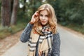 Cute happy young woman in a stylish spring coat in a checkered vintage scarf walks in the park on a warm spring day.