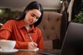 Cute hardworking girl making notes, copying online information , using laptop while working or studying, sitting in cafe Royalty Free Stock Photo