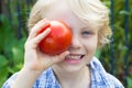 Cute healthy child holding an organic tomato over his eye