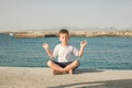 Cute healthy happy smiling little toddler boy child with eyes closed practices yoga & meditating outdoors on sea. Beginner Royalty Free Stock Photo