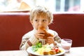 Cute healthy kid boy eating croissant and drinking strawberry milkshake in cafe. Happy child having breakfast with Royalty Free Stock Photo