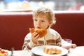 Cute healthy kid boy eating croissant and drinking strawberry milkshake in cafe. Happy child having breakfast with Royalty Free Stock Photo