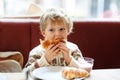 Cute healthy kid boy eating croissant and drinking strawberry milkshake in cafe. Happy child having breakfast with Royalty Free Stock Photo