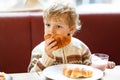 Cute healthy kid boy eating croissant and drinking strawberry milkshake in cafe. Happy child having breakfast with Royalty Free Stock Photo