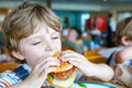 Cute healthy preschool boy eats hamburger sitting in school canteen Royalty Free Stock Photo