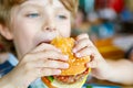 Cute healthy preschool boy eats hamburger sitting in school canteen Royalty Free Stock Photo