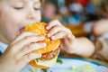 Cute healthy preschool boy eats hamburger sitting in school canteen Royalty Free Stock Photo