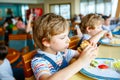 Cute healthy preschool kid boy eats hamburger sitting in school or nursery cafe. Happy child eating healthy organic and Royalty Free Stock Photo