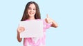 Cute hispanic child girl holding blank empty banner smiling happy and positive, thumb up doing excellent and approval sign Royalty Free Stock Photo