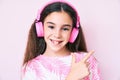 Cute hispanic child girl listening to music using headphones smiling cheerful pointing with hand and finger up to the side Royalty Free Stock Photo