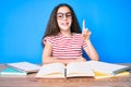 Cute hispanic child girl studying for school exam sitting on the table smiling with an idea or question pointing finger up with