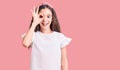 Cute hispanic child girl wearing casual white tshirt doing ok gesture with hand smiling, eye looking through fingers with happy Royalty Free Stock Photo