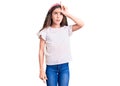 Cute hispanic child girl wearing casual white tshirt making fun of people with fingers on forehead doing loser gesture mocking and Royalty Free Stock Photo