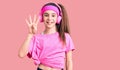 Cute hispanic child girl wearing gym clothes and using headphones showing and pointing up with fingers number four while smiling Royalty Free Stock Photo