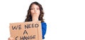 Cute hispanic child with long hair holding we need a change banner covering mouth with hand, shocked and afraid for mistake