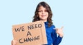 Cute hispanic child with long hair holding we need a change banner pointing finger to one self smiling happy and proud