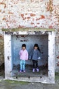 Cute identical twins sisters while playing and hiding inside a small stone storage area with old brick walls