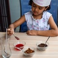Cute Indian chef girl preparing sundae dish as a part of non fire cooking which includes vanilla ice cream, brownie, coco powder,