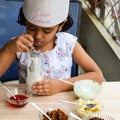 Cute Indian chef girl preparing sundae dish as a part of non fire cooking which includes vanilla ice cream, brownie, coco powder,