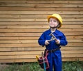 Cute inquisitive boy in blue overalls and a construction helmet with repair tools in his hands