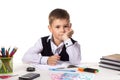 Cute intelligent pupil sitting at the desk with hand under the chin surrounded with stationery