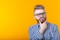 Cute intelligent young man with a beard and with glasses poses on a yellow background with copy space and thinks about