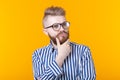 Cute intelligent young man with a beard and with glasses poses on a yellow background and thinks about something. The