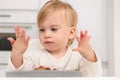 Cute interested caucasian blonde child eat fresh fruits,food,look at messy,dirty hand on background of light kitchen