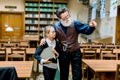 Cute interested teen schoolgirl holding a big book and listening her intelligent senior bearded grandfather or librarian