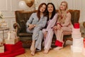 Cute interracial young girls in pajamas are sitting on sofa in room among gift boxes.