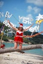 Cute joyful woman jumps in red dress, sunglasses and santa hat on exotic tropical beach. Holiday concept for New Years Royalty Free Stock Photo