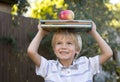 cute joyful 6 year old boy is holding a stack of books and a big apple on his head Royalty Free Stock Photo