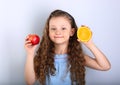 Cute joying smiling kid girl with curly hair style holding citrus orange fruit and red apple in the hands on blue background Royalty Free Stock Photo