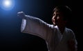 Cute karate boy in white kimono isolated on dark background. Child ready for martial arts fight. Kid fighting at judo training. Royalty Free Stock Photo