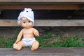 Cute kewpie doll sits on wooden bench in country house yard