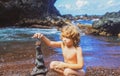 Cute kid boy making stack stones on the coast of the sea in the nature. Cairn on the ocean beach, five pebbles tower Royalty Free Stock Photo