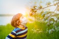 Cute kid boy in medical face mask in flowering apple trees tying to smell flowers. Happy caucasian child in park at