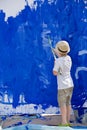 Cute kid boy in straw hat painting fence with blue color. Child drawing outdoors