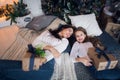 Cute kid girl and her mom playing under christmas tree with presents, lying on wooden floor in room. Wearing trendy Royalty Free Stock Photo