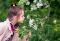 Cute kid girl in a light pink coat sniffs apple tree flowers in spring