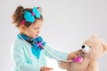 Cute kid girl playing doctor with medical headphones and her plush toy at home