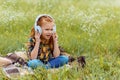 cute kid listening music in headphone while sitting on blanket in field Royalty Free Stock Photo